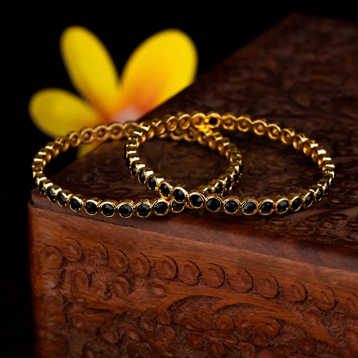 Pair of gold-tone bangles with round black accents arranged on a carved brown box