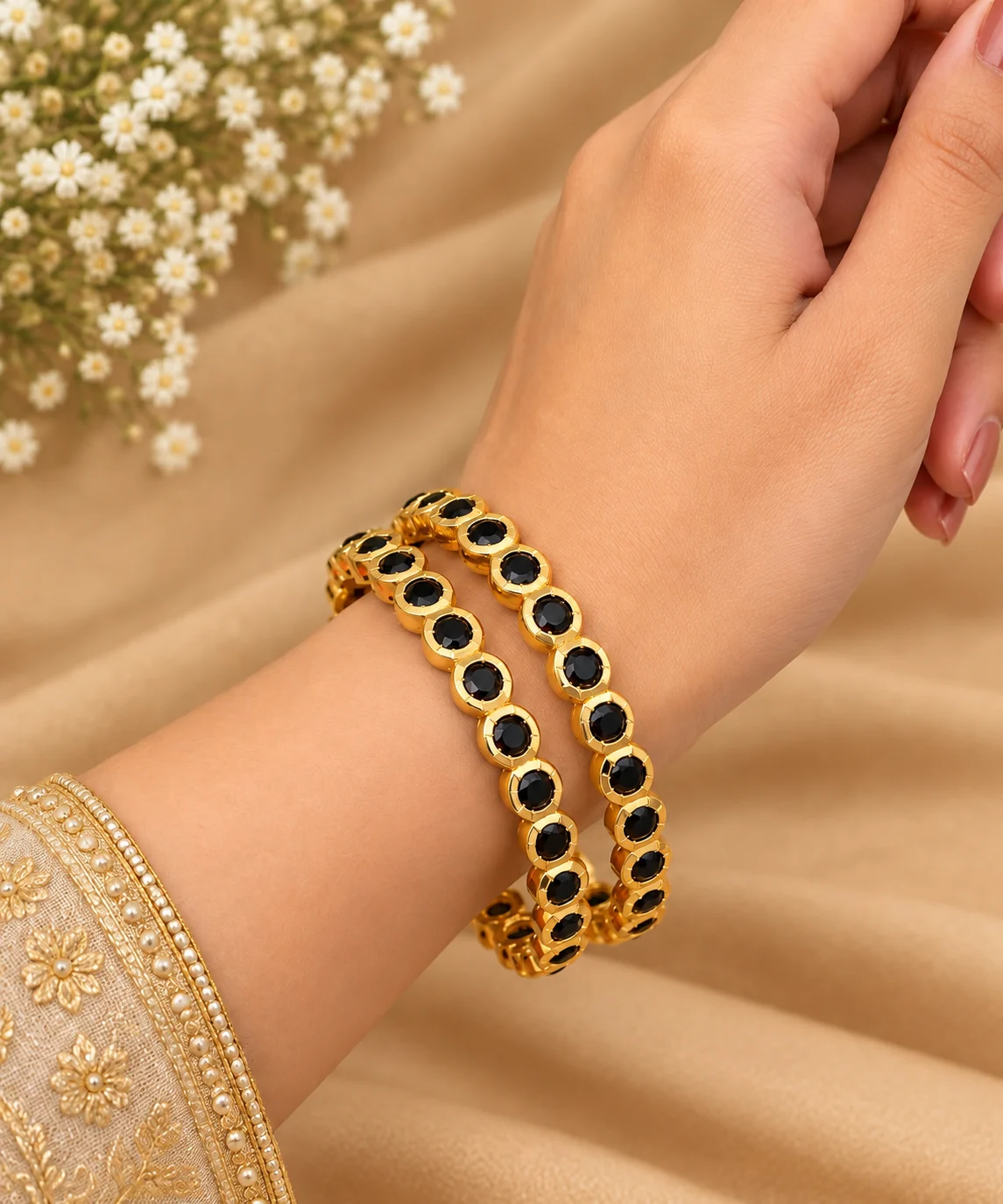 Pair of gold-tone bangles with round black accents worn on a wrist