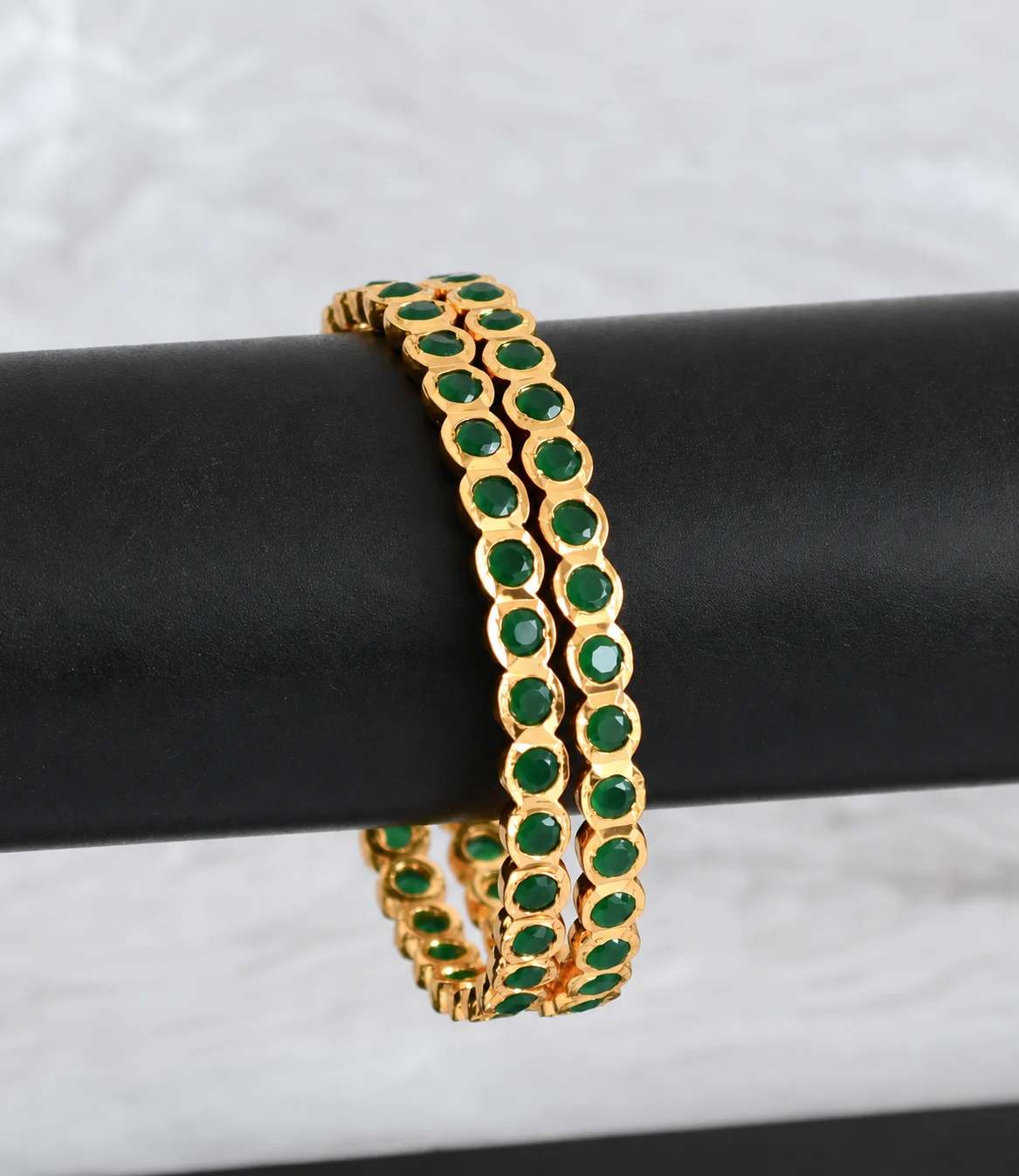 Pair of gold-tone bangles with round green accents draped over a black display bar